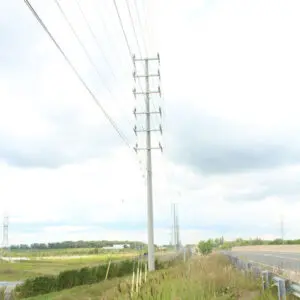 Utility Pole - Road Crossing A spun concrete utility pole with a 'road crossing' application. Project is in a grassy, flat area next to a highway.