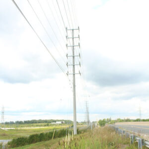Utility Pole - Road Crossing A spun concrete utility pole with a 'road crossing' application. Project is in a grassy, flat area next to a highway.